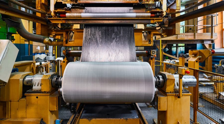 Rolling reinforced rubber sheet on metal reel drum in plant workshop closeup. Production line at tire manufacturing factory. Modern technology