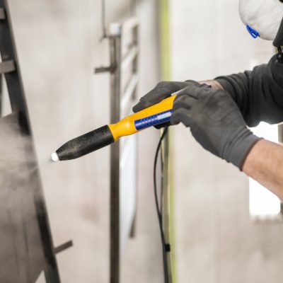 The detail of a man working in a factory finishes a job using the technique of electrostatic powder coating with a spray gun.