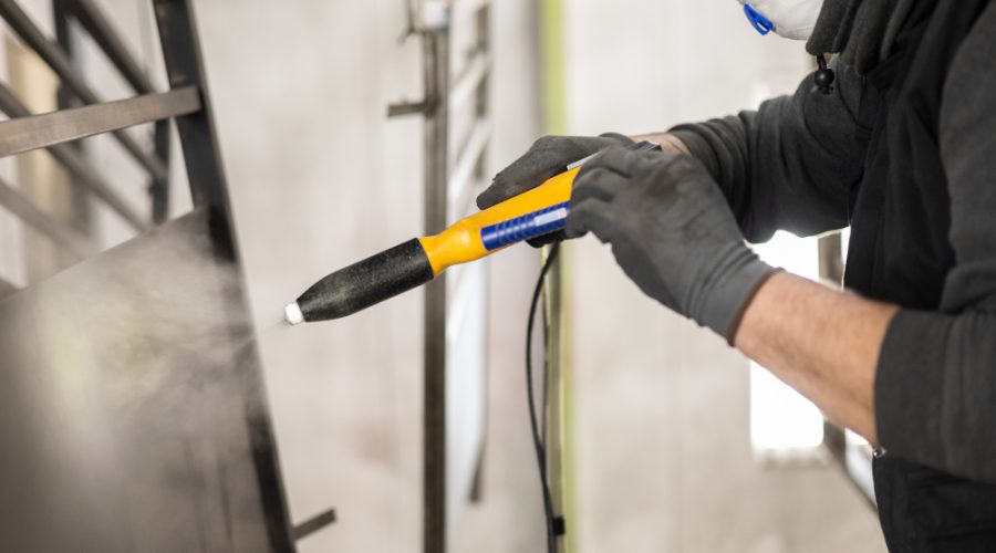 The detail of a man working in a factory finishes a job using the technique of electrostatic powder coating with a spray gun.