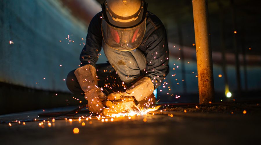 Male worker metal cutting spark on tank bottom steel plate with flash of cutting light close up wear protective gloves and mask in side confined space.